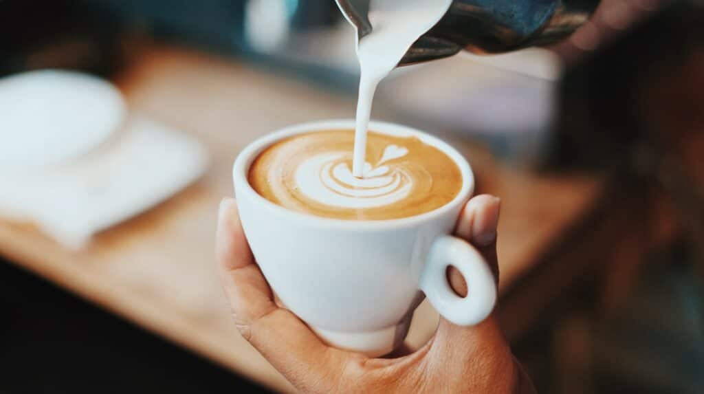 A barista pouring hot milk into a coffee