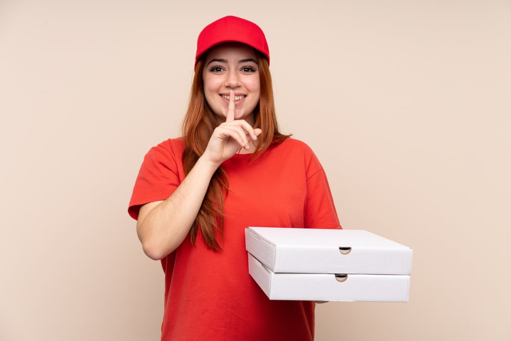 Girl holding pizza and making a silence gesture