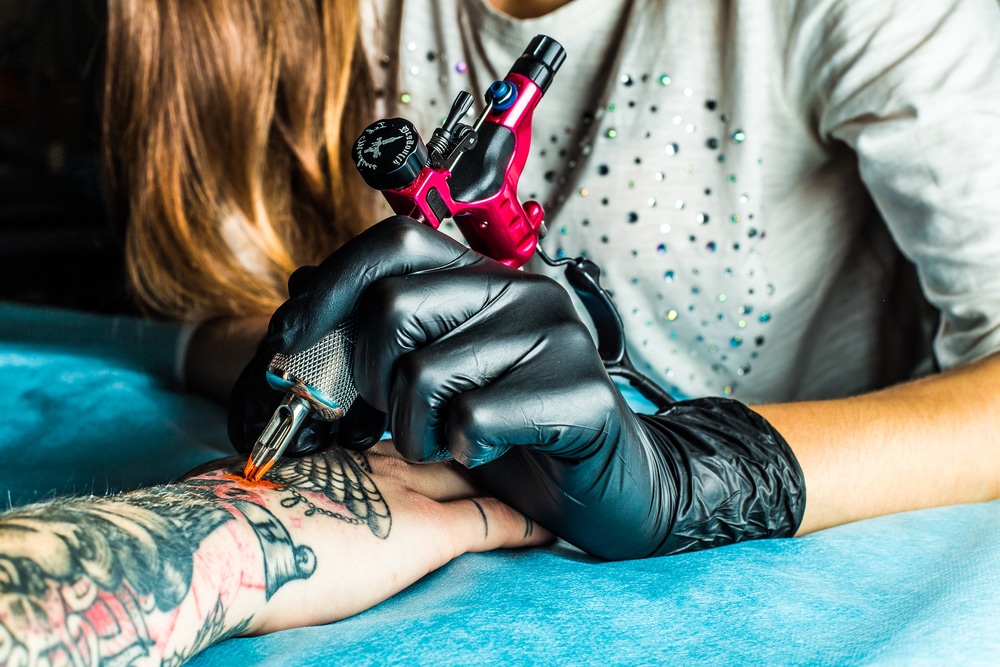Tattoo artist holding a pink tattoo machine in black sterile gloves