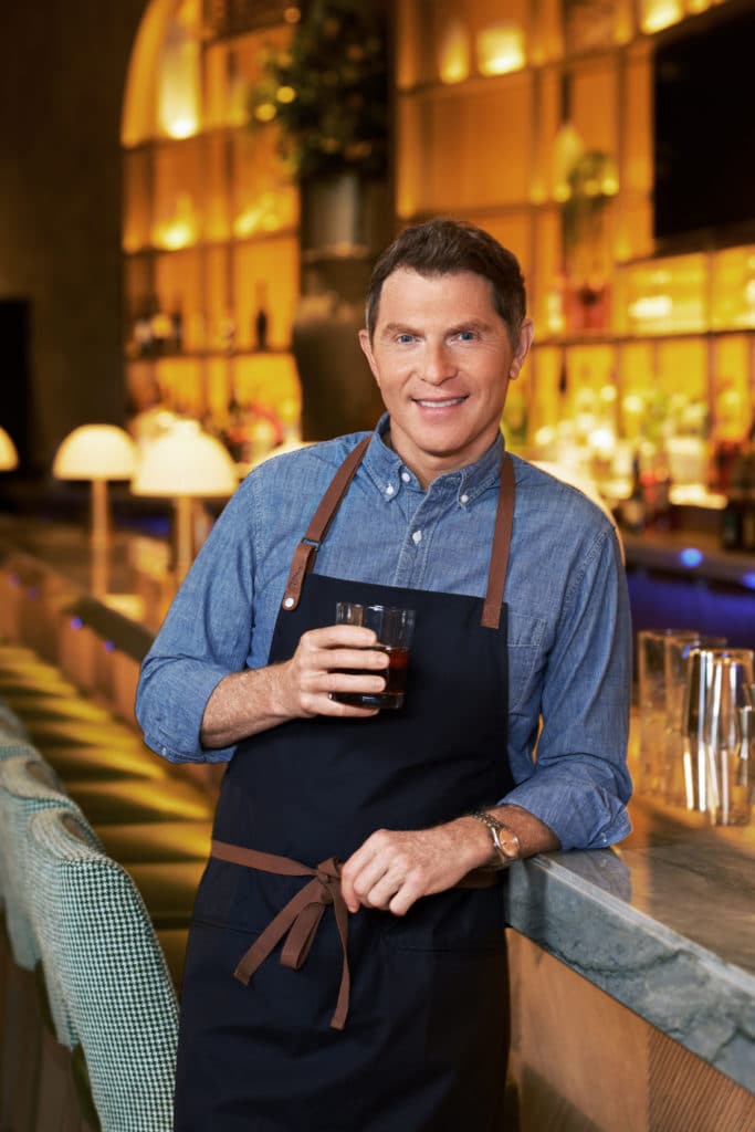Bobby Flay holding a drink in an apron