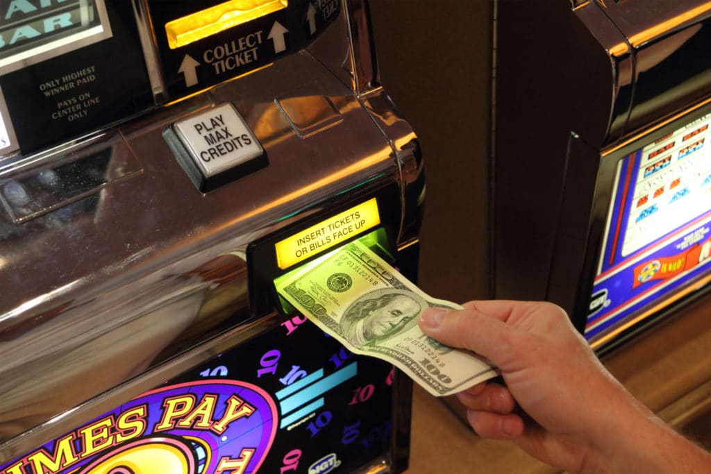 a hand putting $100 inside a slot machine