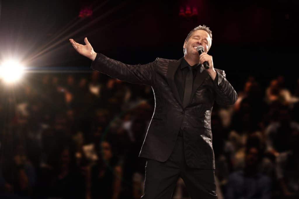 Terry Fator on stage wearing a black suit with a microphone