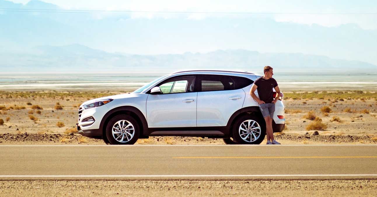 A man standing next to a car in the desert