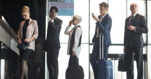 A group of business professionals carries various luggage as they wait in line to board a plane.