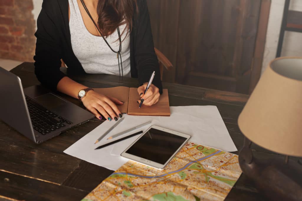 girl sitting at a desk with a map on it, writing in a journal