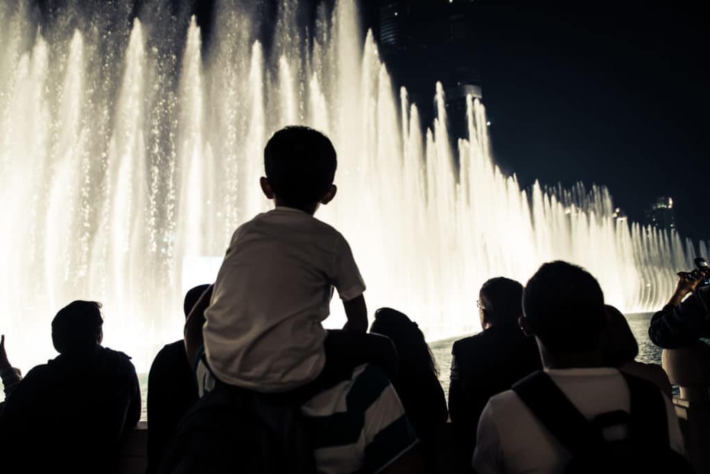 a small child on a man's shoulders looking at the Fountains of Bellagio