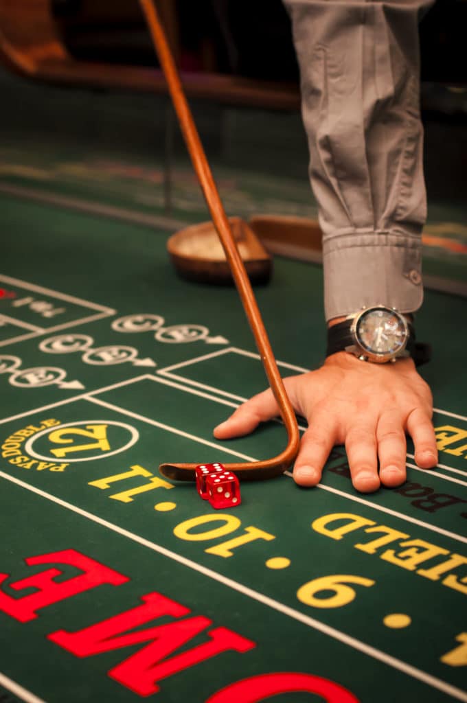 a man's hand with a luxury watch pushing dice on a craps table