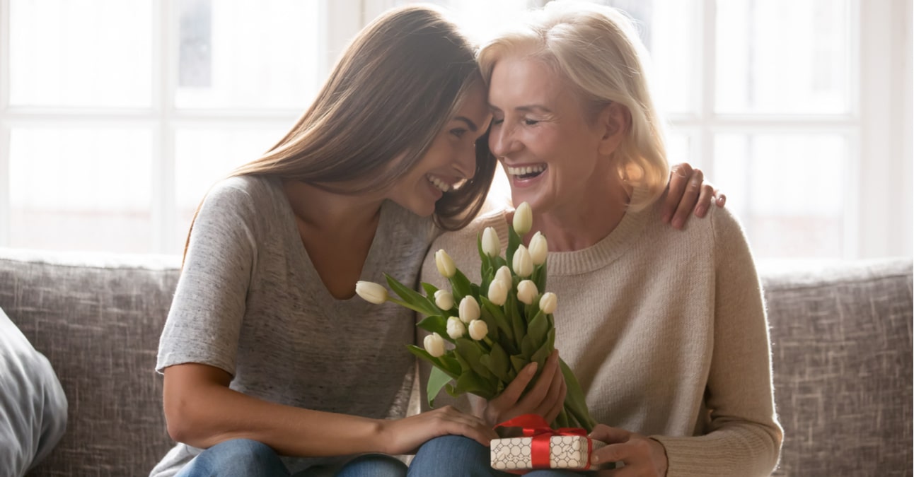 a daughter hugging her mother with flowers and a presenti her hand on Mother's Day