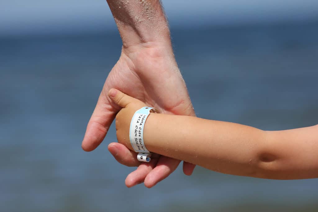 a parent holding a child's hand with phone numbers written on a white wristband around the child's wrist