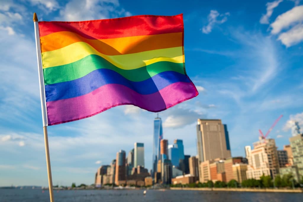 a rainbow flag set against the New York skyline during the daytime