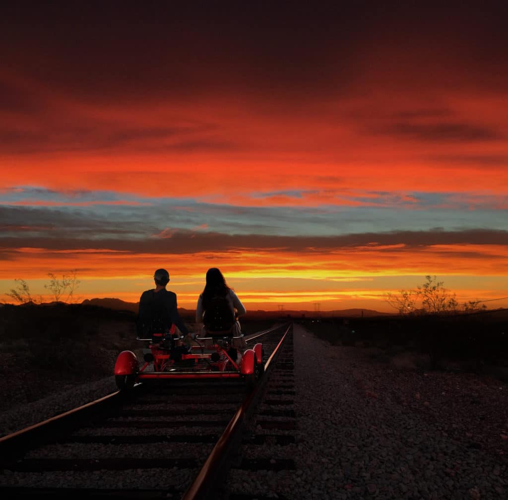two people on railroad tracks riding into the sunset