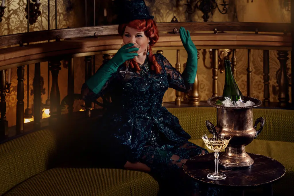 a woman with green gloves drinking a cocktail in a booth