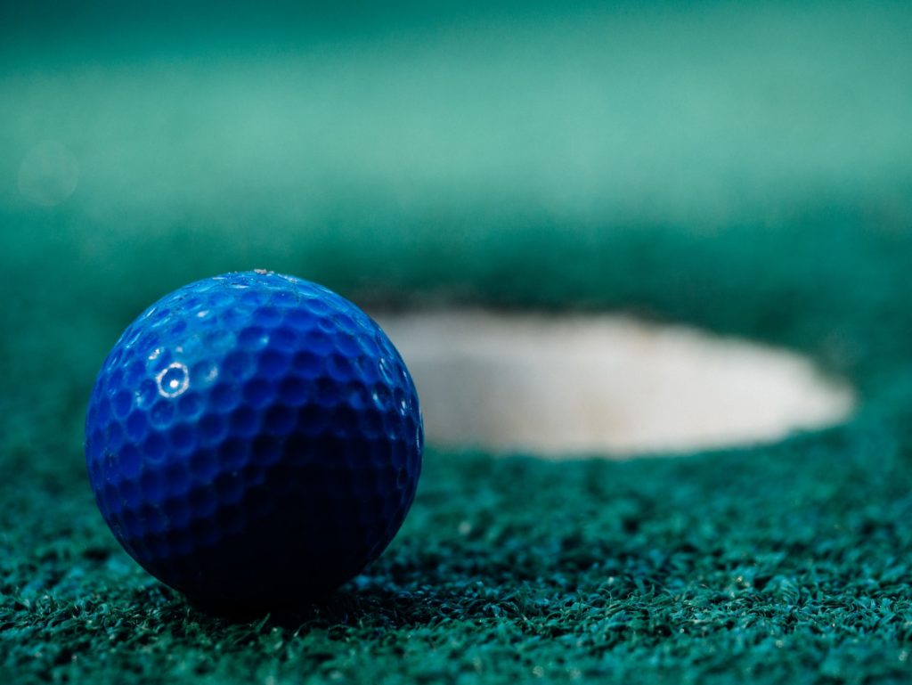 A blue golf ball next to it's hole