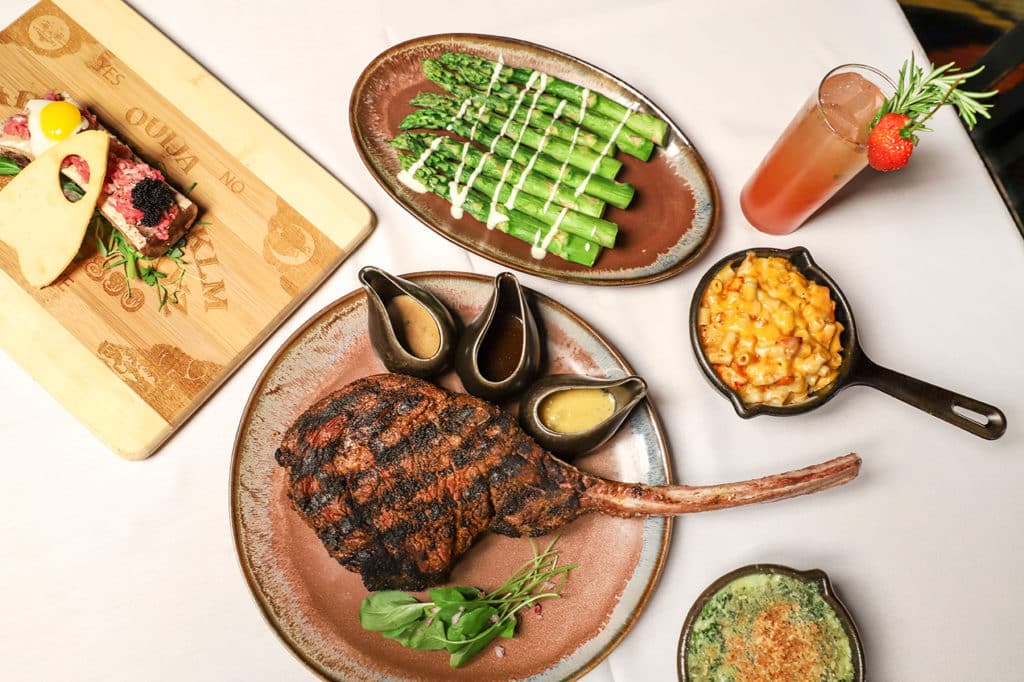 a tomahawk steak with side dishes next to a cutting board with sides