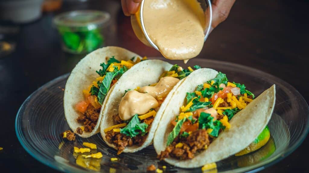 A server pouring sauce on tacos