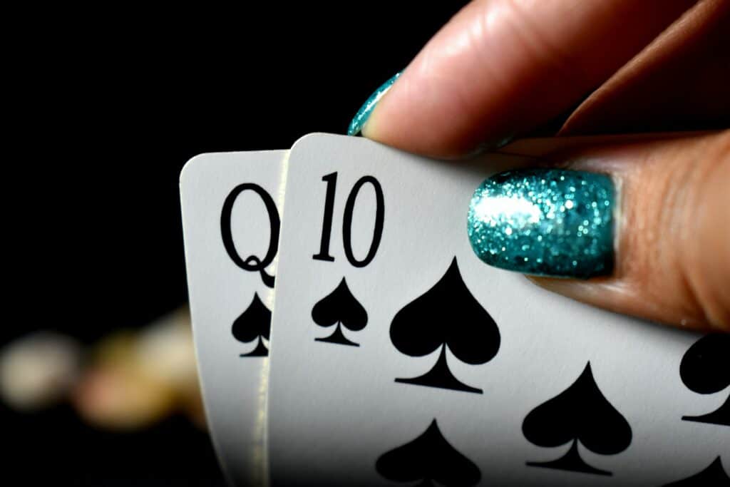Image of a lady holding two playing cards, wearing glittery turquoise nail varnish
