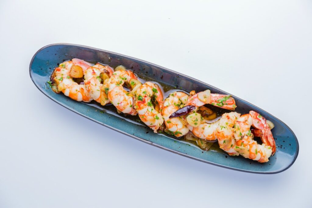 Beautifully cooked blue rock shrimp paired with fresh spring greens, served on a navy plate.