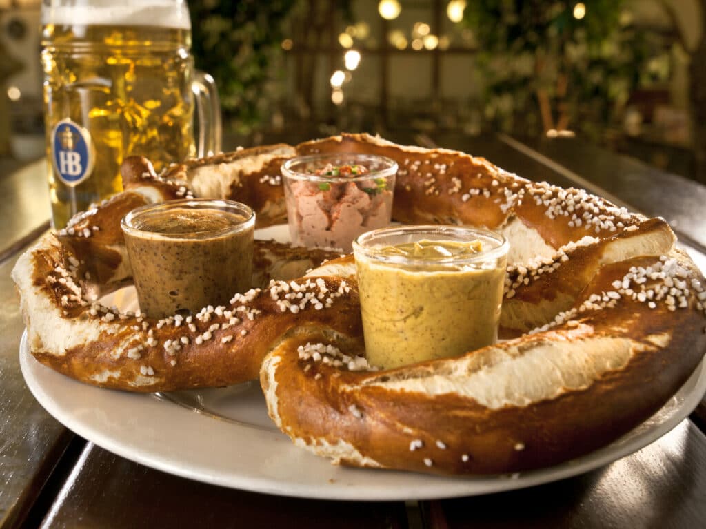 A large, salted soft pretzel with three types of mustards on a plate.