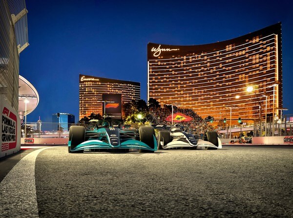 Two F1 cars at night with the Wynn and Encore hotels in the back
